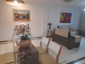 Un saló amb un sofà, una taula de dinar amb cadires, un vas de flors i dos quadres a les parets.