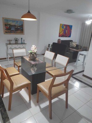 A dining area with a glass-top table, wooden chairs, and a hanging pendant light.