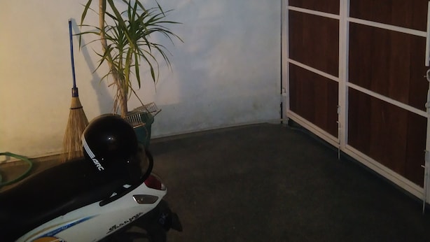 A covered outdoor area with a scooter, a broom, and a potted plant.