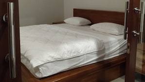 A bedroom with a wooden bed, white bedding, and a door with a key lock. - Lily house bali (denpasar selatan)