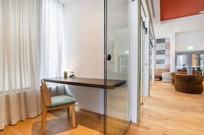 A modern room with a glass partition, a wooden desk, a green chair, and a brown sofa. - The Crosby 2BR Luxury Palermo Home (Miami)