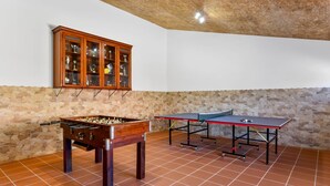 A room with a foosball table, a ping pong table, and a trophy cabinet against a stone wall. - Apartment 'Quarto 7' with Wi-Fi and Air Conditioning (Corte do Pinto)