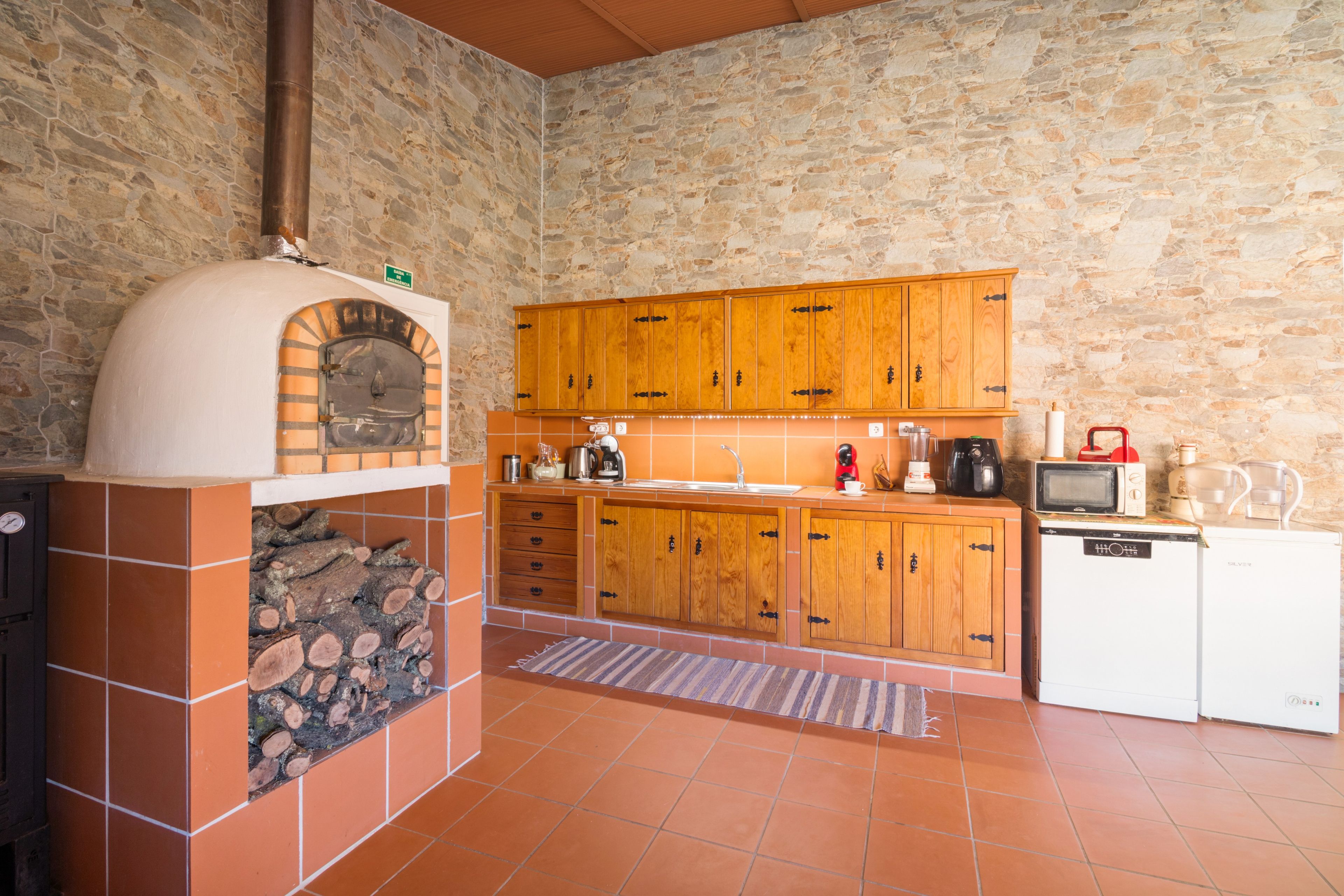 Eine Küche mit Steinwand, Holzschränken, einem eingebauten Ofen und einem kleinen Kühlschrank.