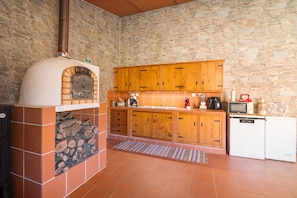 Una cocina con pared de piedra, armarios de madera, horno empotrado y un refrigerador pequeño.