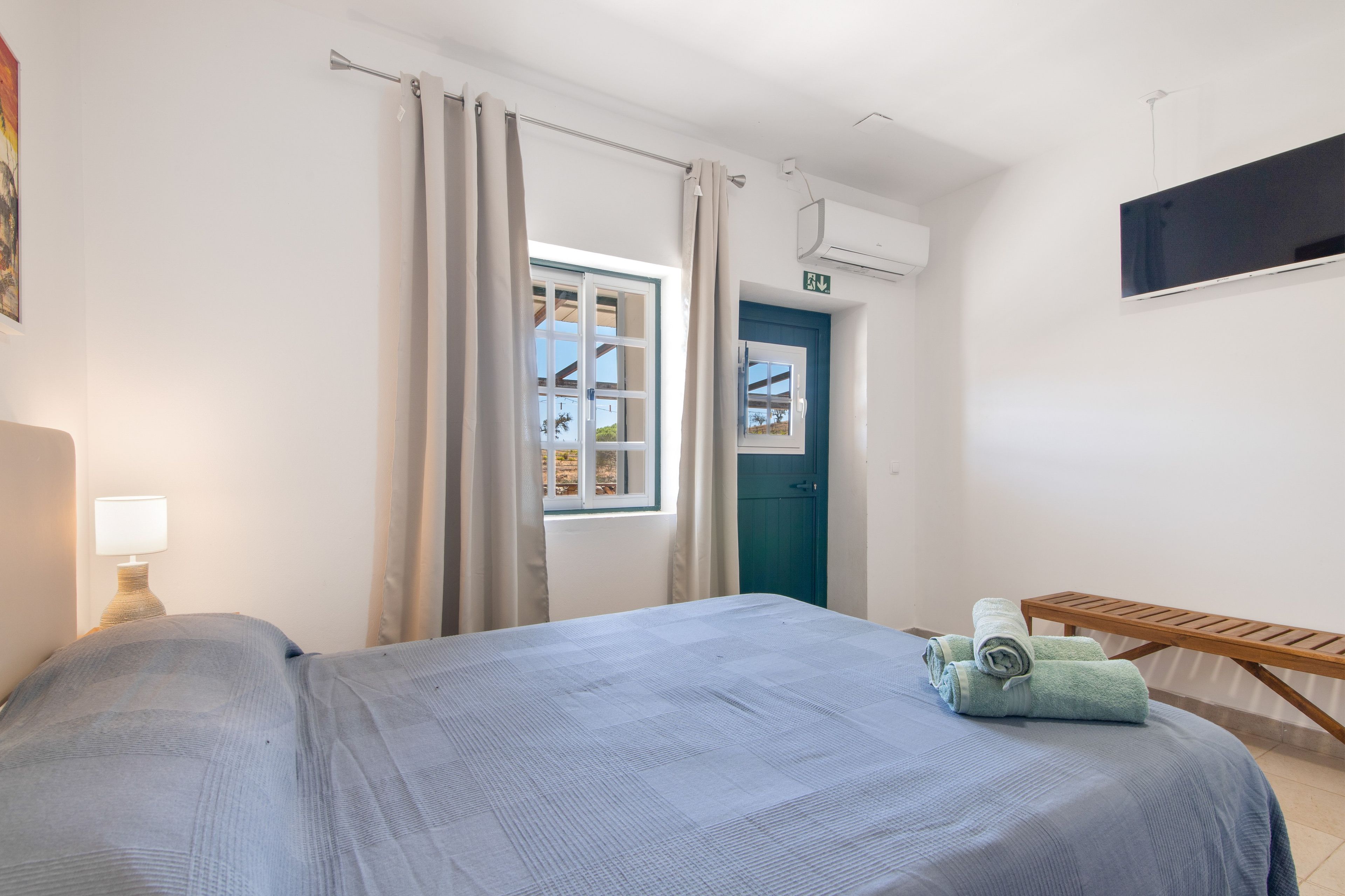 Ein Schlafzimmer mit Bett, Fenster, Tür und einem kleinen Tisch mit Handtüchern.