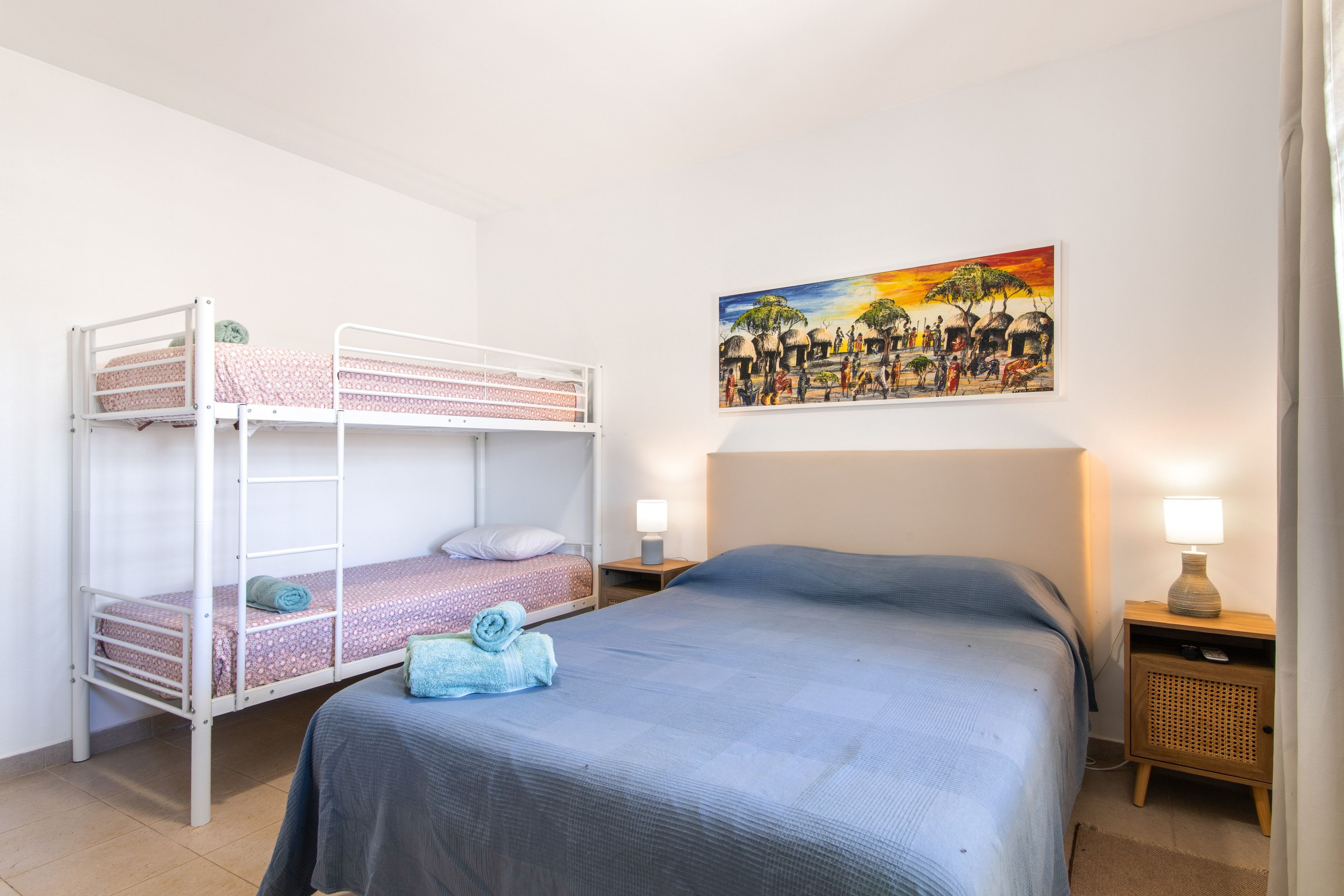 Una habitación con literas, una cama individual, un cuadro en la pared y lámparas de noche.