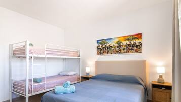 Una habitación con literas, una cama individual, un cuadro en la pared y lámparas de noche.