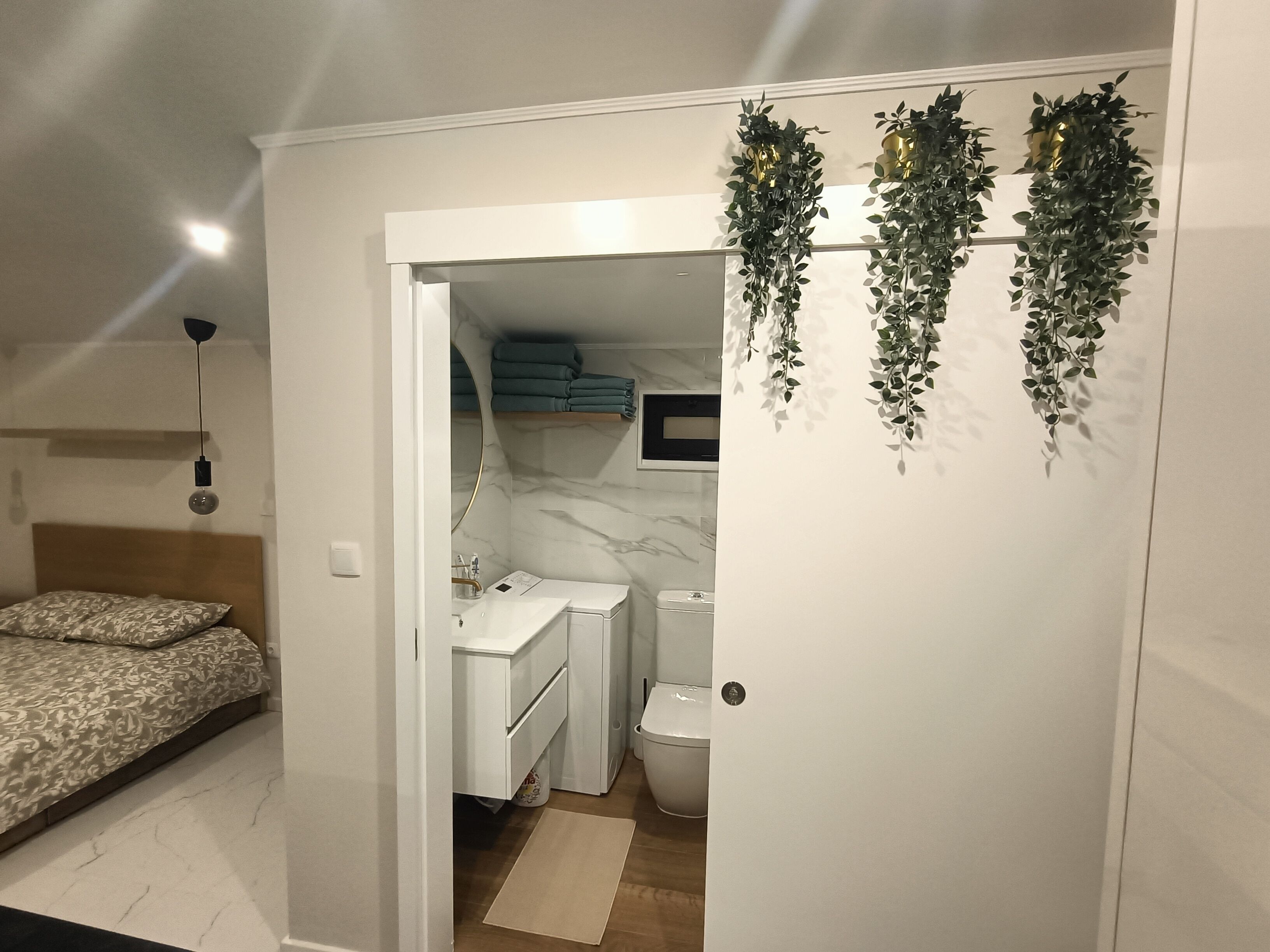 Een slaapkamer met een bed, een badkamer met toilet, wastafel en spiegel, en een gang met een deur naar de badkamer.