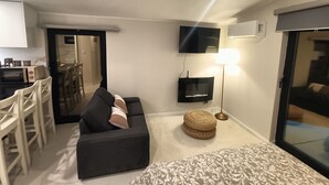 Ein kompakter Wohnbereich mit einer Couch, einem Fernseher, einer Lampe und einer Küchenzeile.