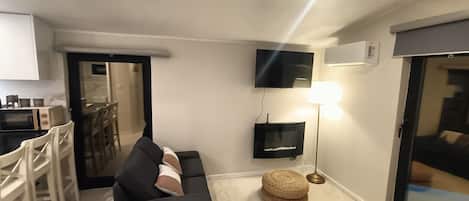 Un espacio habitable compacto con sofá, televisión, lámpara y una zona de kitchenette.