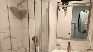 Ein Badezimmer mit einer gläsernen Dusche, einem weißen Waschbecken mit goldfarbenen Armaturen und einem Spiegel darüber.