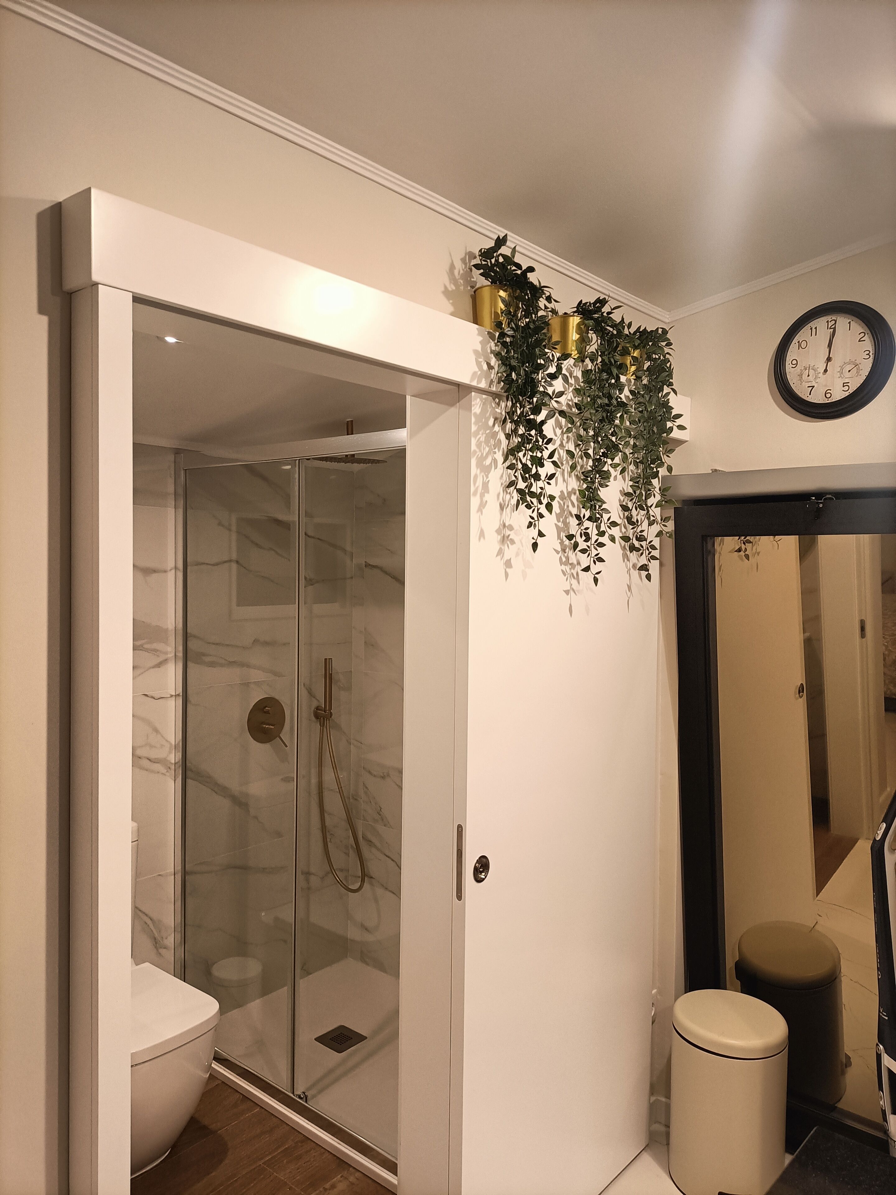 A modern bathroom with a glass-enclosed shower, a toilet, and a trash bin.