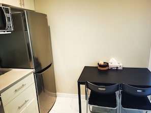 Een kleine keuken met een koelkast, een magnetron en een eettafel met stoelen.