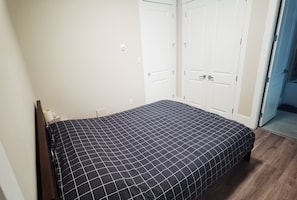 Een slaapkamer met een bed, witte muren en een deur naar een andere kamer.