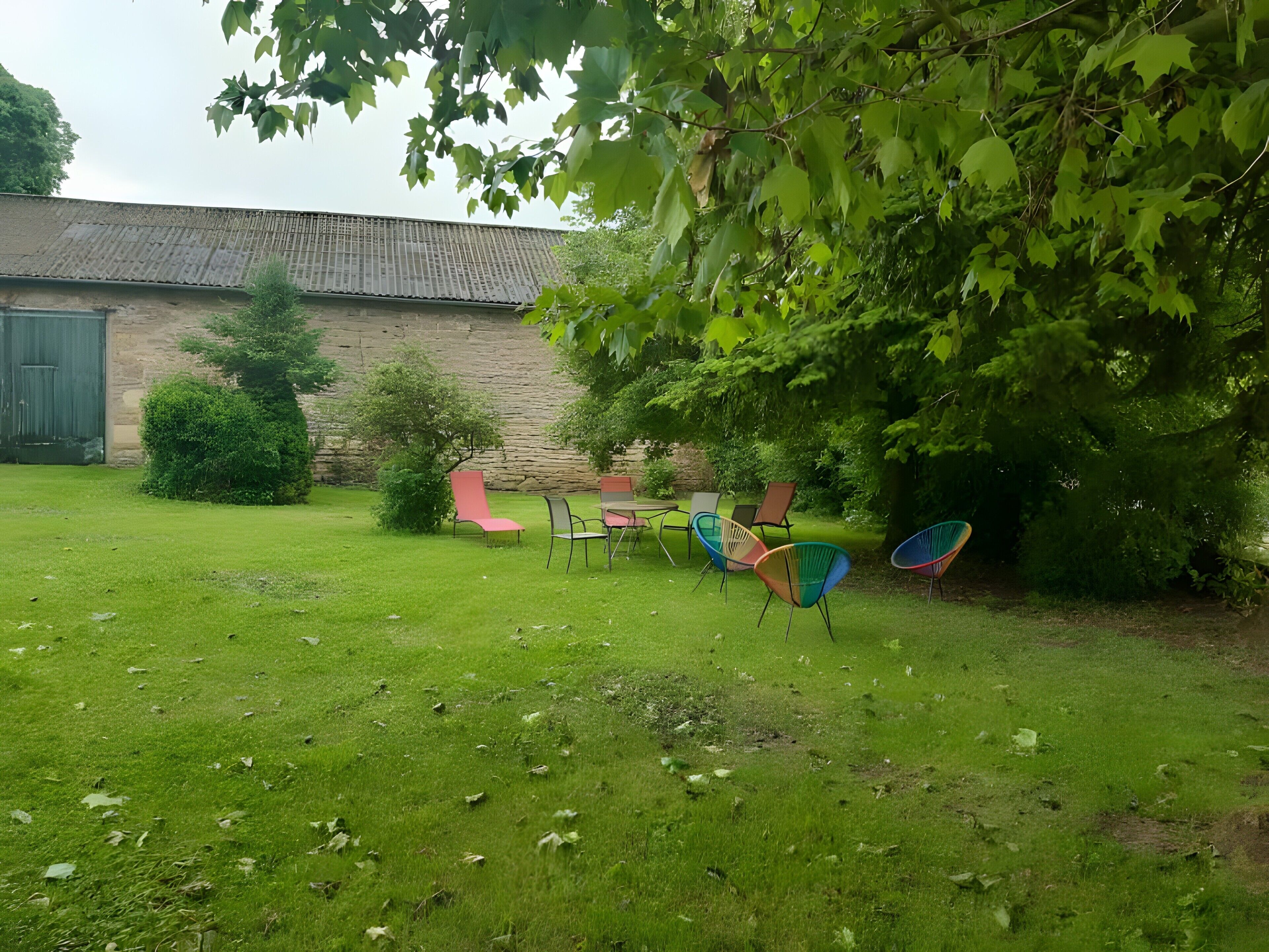 Un espace extérieur verdoyant, avec un mur de pierre, un arbre et plusieurs chaises colorées.