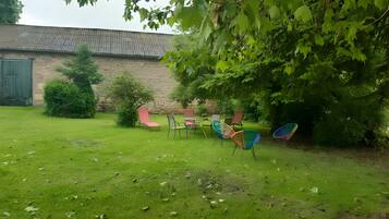 Un espace extérieur verdoyant, avec un mur de pierre, un arbre et plusieurs chaises colorées.