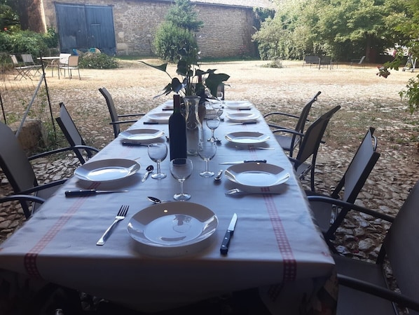 A table set for dining outdoors with chairs, plates, cutlery, and a bottle of wine.