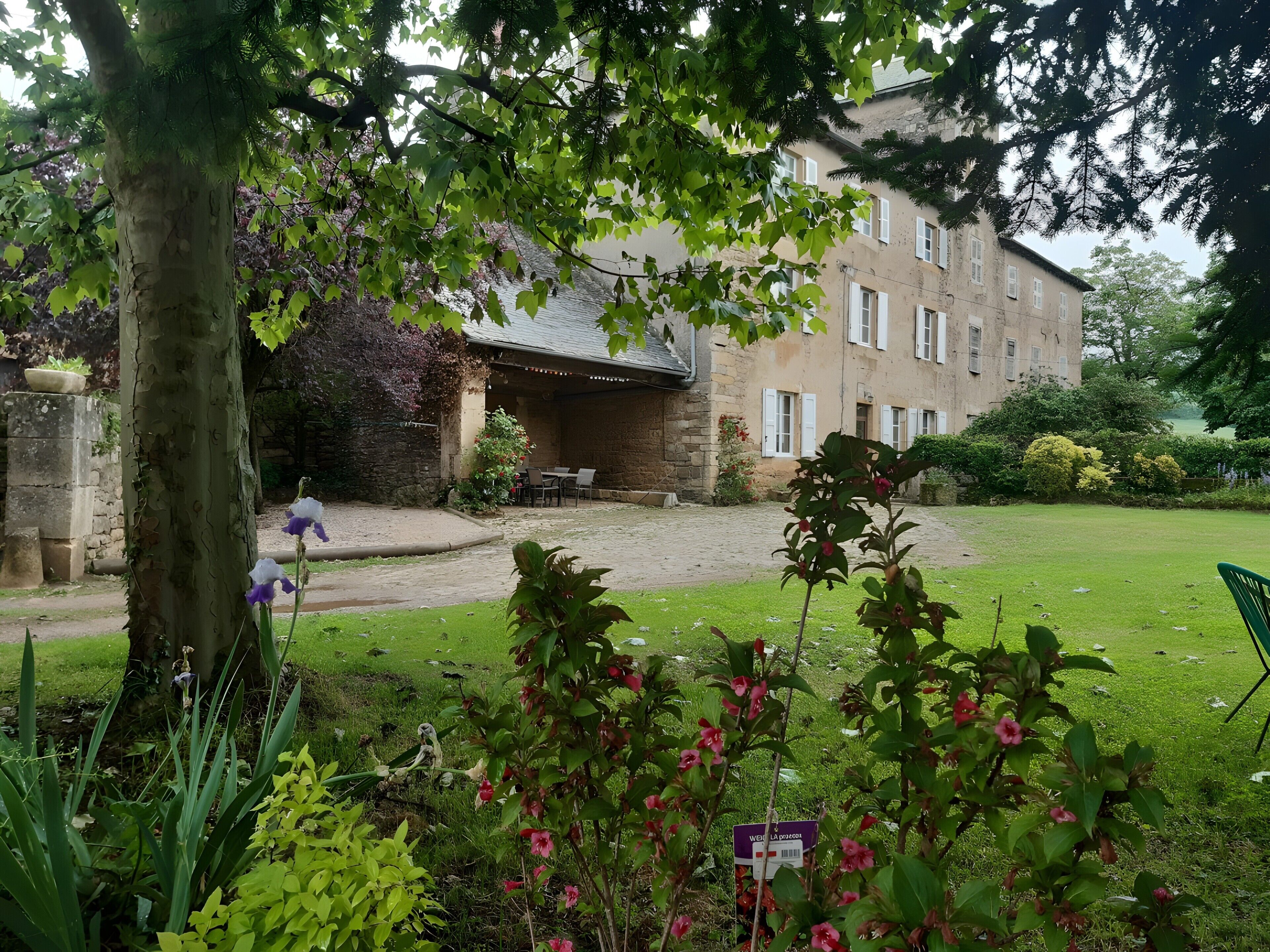 Un bâtiment doté d’une façade en pierre, d’un patio couvert et d’une cour verdoyante.