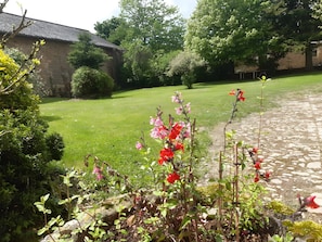 A stone building with a thatched roof, surrounded by a well-maintained lawn and flowering plants.