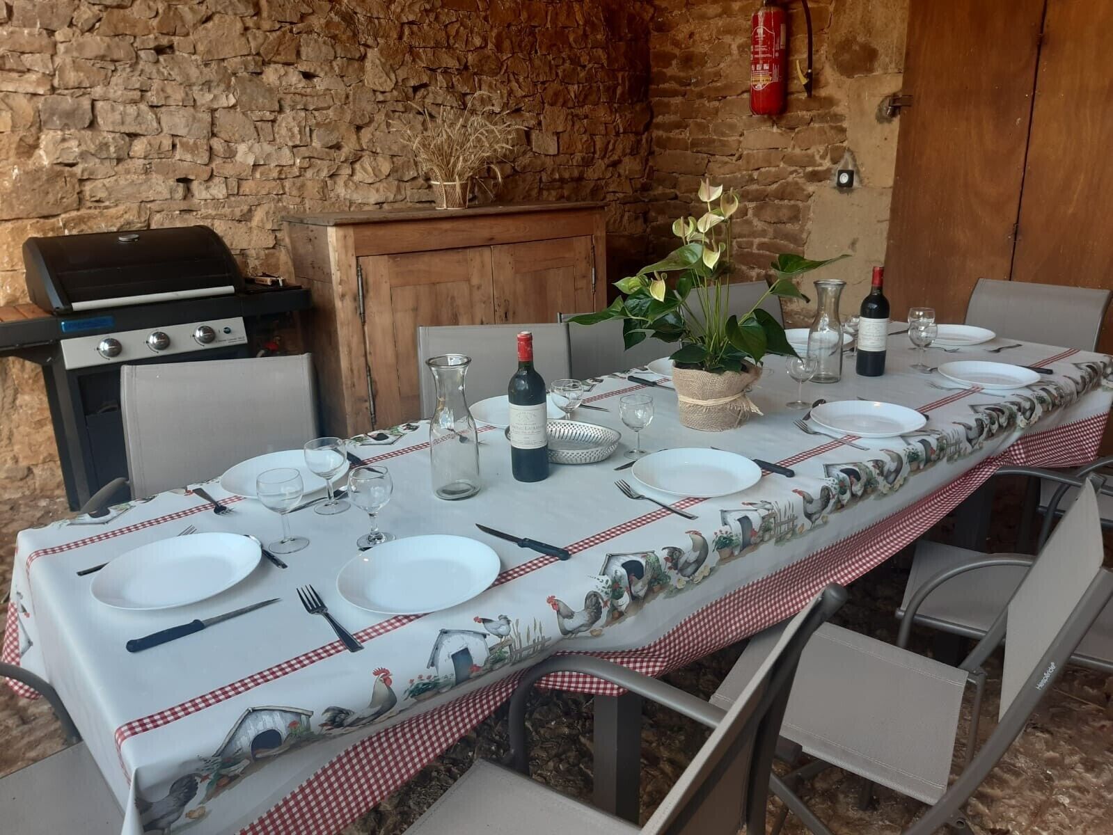 An outdoor dining area with a stone wall backdrop, a grill, and a table set for a meal.