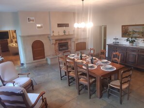 A dining room with a fireplace, wooden dining table set for six, and a kitchen area with cabinets and a countertop.