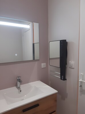 Casa de banho com lavatório branco, espelho e dispensador de toalhas preto.