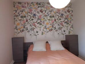 A bedroom with a bed, two nightstands, a wardrobe, and a floral tapestry on the wall.