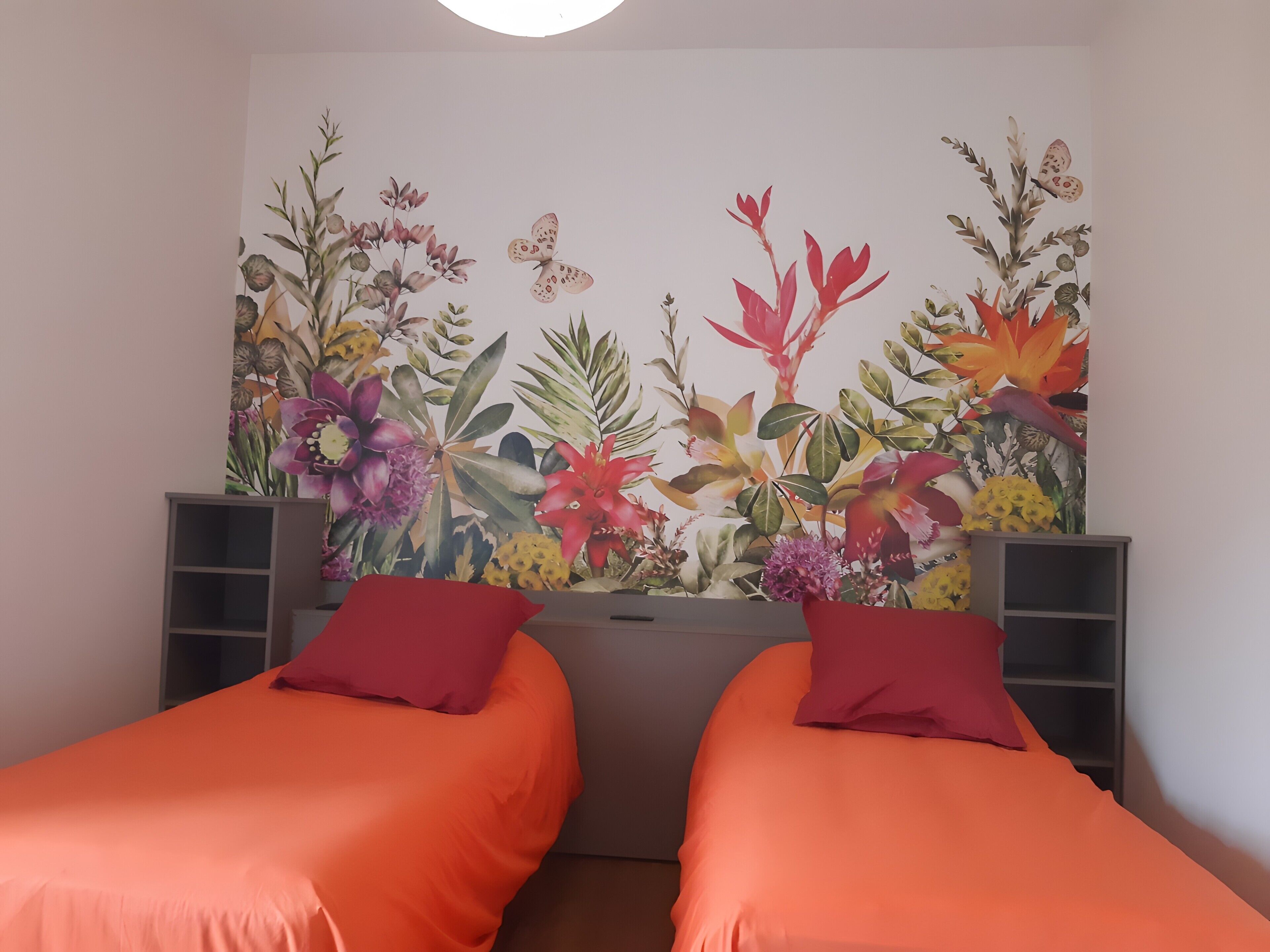 Une chambre avec deux lits, chacun recouvert d’une couverture orange et agrémenté d’un oreiller rouge.