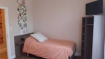 Une chambre avec un lit simple, une armoire et un téléviseur.