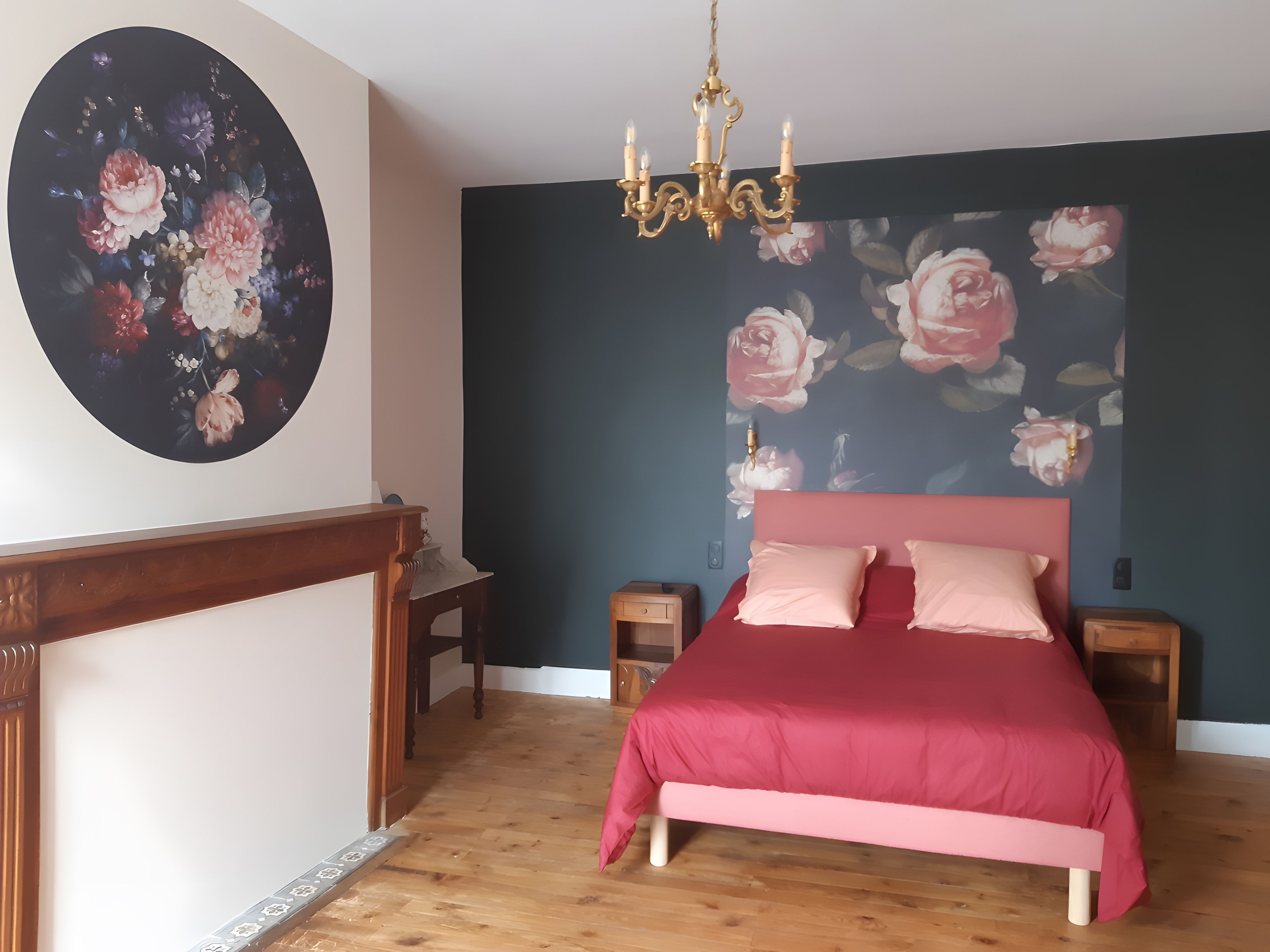 Een slaapkamer met een bed, een nachtkastje, een dressoir, een kroonluchter en een bloemen behang.