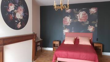 Een slaapkamer met een bed, een nachtkastje, een dressoir, een kroonluchter en een bloemen behang.