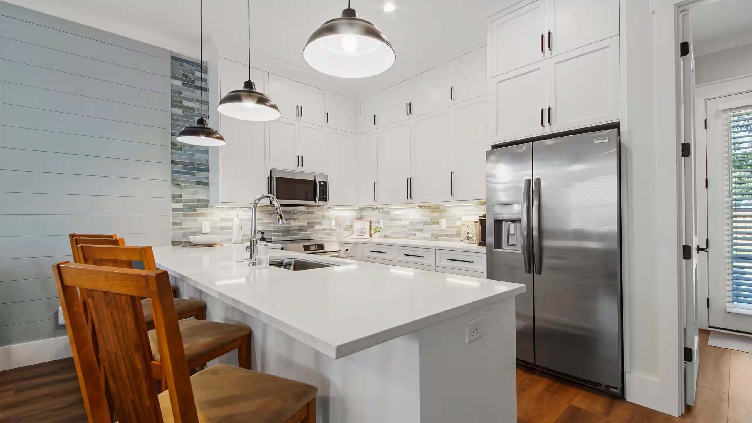 Une cuisine moderne avec des meubles blancs, des appareils en acier inoxydable et un îlot central doté de tabourets de bar.