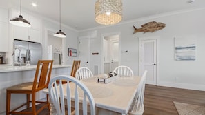 A modern kitchen with stainless steel appliances, a dining area with a wooden table and white chairs, and a decorative fish on the wall. - Laguna Dreamin' 226-Private Pool-Sleeps 10 (Panama City Beach)