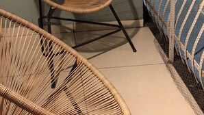 A wicker chair with a metal frame on a balcony with a view of a street and buildings.