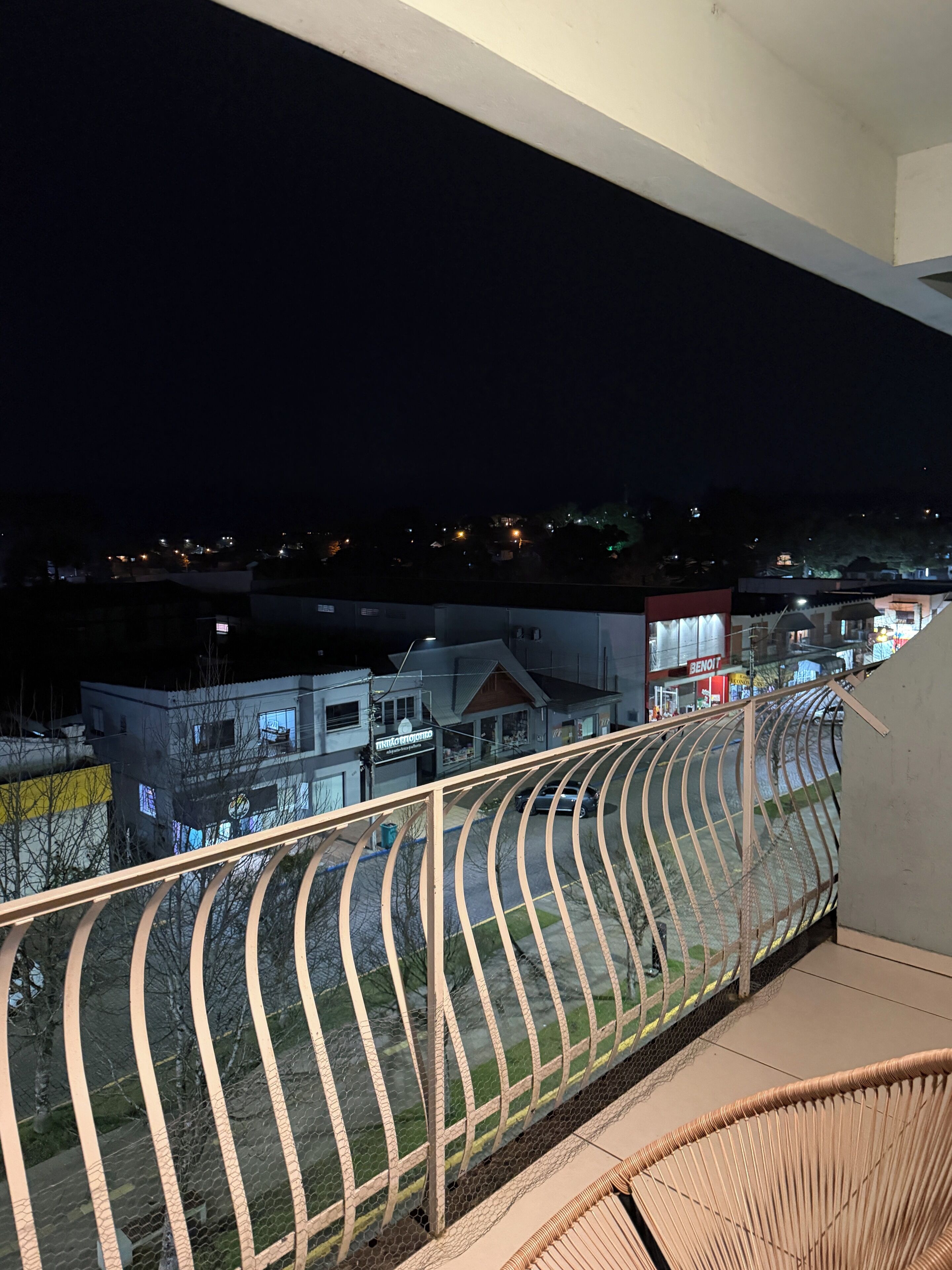 Uma varanda com grades de metal curvas voltada para uma área residencial à noite.