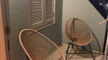 A room with two wicker chairs, a window with shutters, and a staircase leading to an upper level.