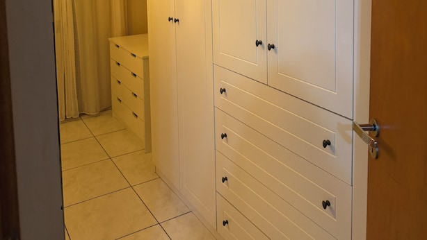 A walk-in closet with white cabinetry and multiple drawers.