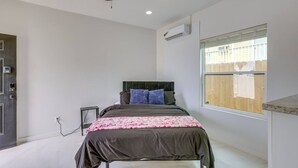 A bedroom with a bed, a ceiling fan, an air conditioning unit, a window with blinds, and a door with a lock. - #10 | Clean Pet-Friendly Studio | Pool | Parking (South Padre Island)
