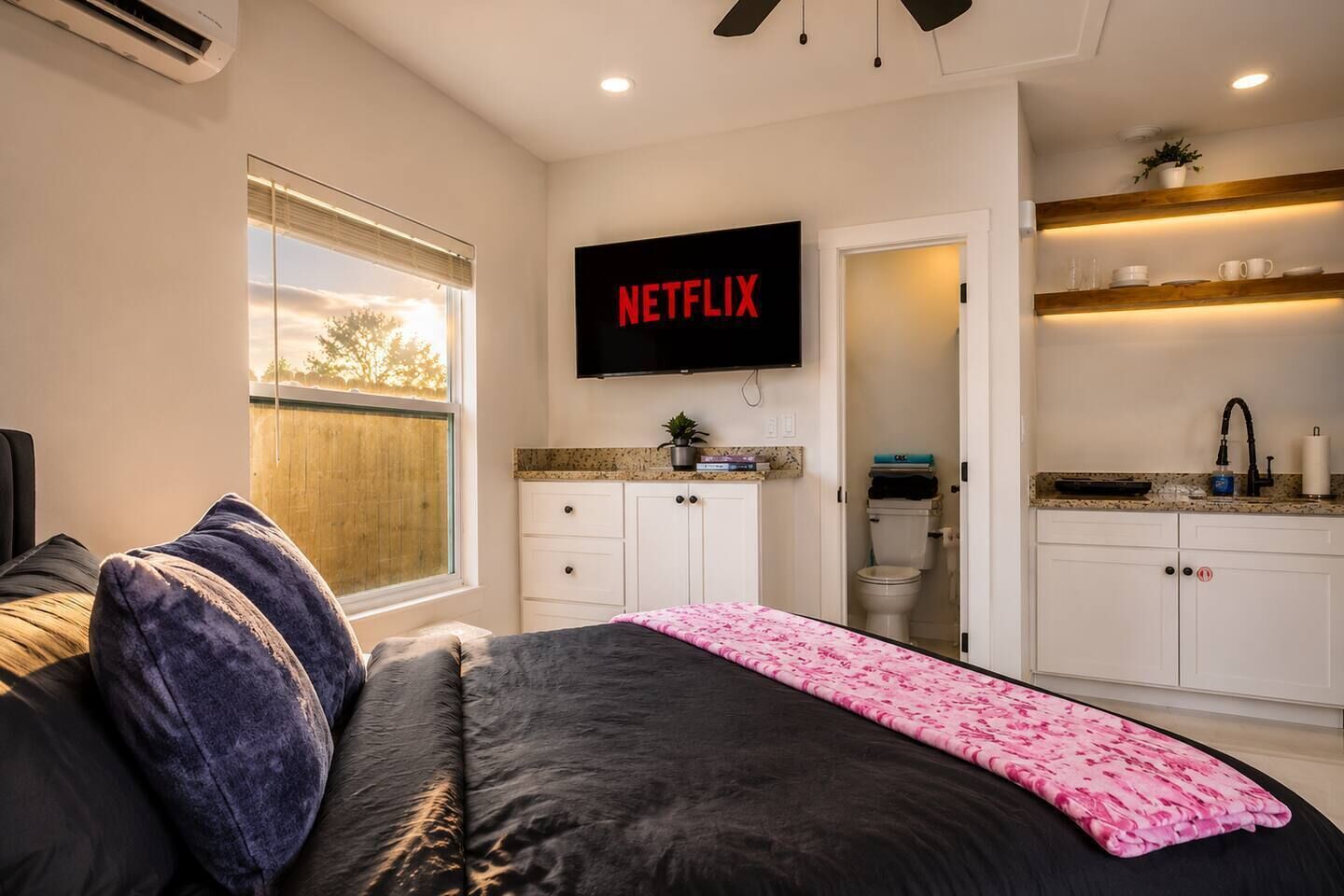 Ein Schlafzimmer mit einem Bett, einem an der Wand befestigten Fernseher und einem Fenster.