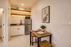 A compact kitchen with a refrigerator, a dining table set for two, and a wall-mounted light fixture. - #10 | Clean Pet-Friendly Studio | Pool | Parking (South Padre Island)