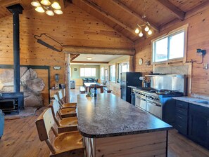 L’intérieur d’une cabane en bois comprend un îlot central, des bancs en bois, un poêle et un coin cuisine équipé d’appareils électroménagers.