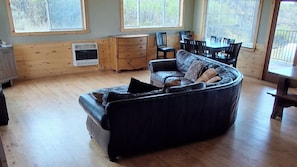 A cozy living room with a curved black sofa, wooden flooring, a small wooden cabinet, and a dining area with chairs and a table.