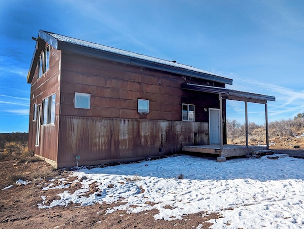 Une cabane en bois rustique, dotée d’une véranda, d’une porte et d’une petite fenêtre.