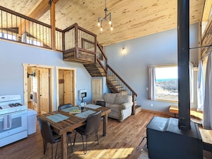 Un vaste espace de vie agrémenté d’un escalier en bois, d’une table à manger avec des chaises, d’un canapé et d’une grande fenêtre offrant une vue dégagée.