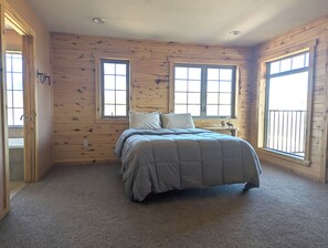 A bedroom with a bed, two windows, a wooden wall, and a carpeted floor.