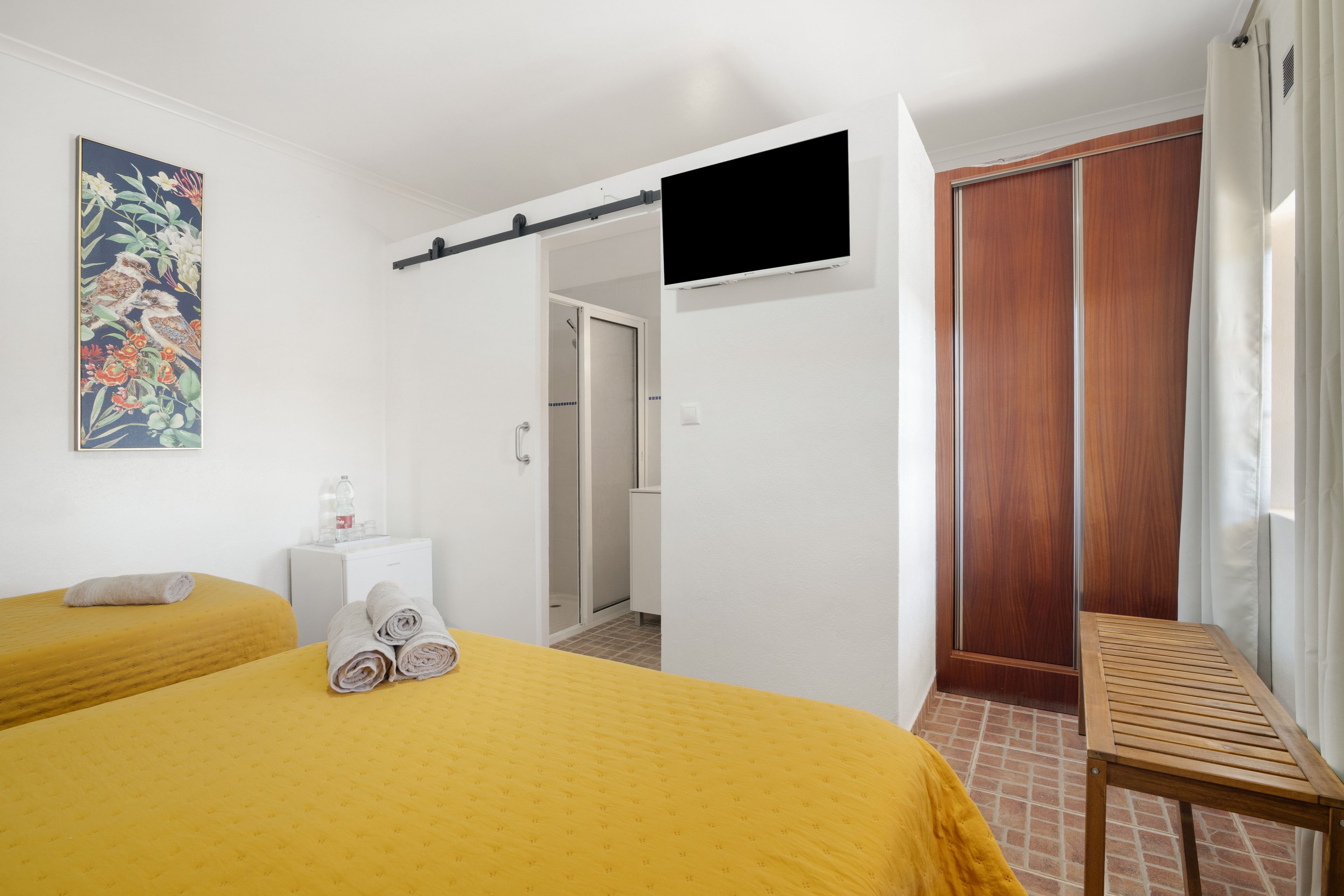 Habitación de hotel con dos camas, televisor, ducha y un banco de madera.