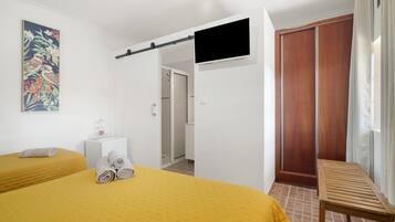 Habitación de hotel con dos camas, televisor, ducha y un banco de madera.