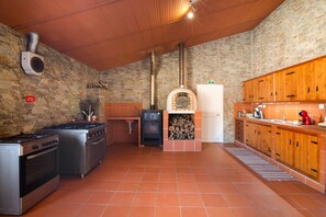 A kitchen with a stone wall, a wood stove, a gas stove, and a sink.