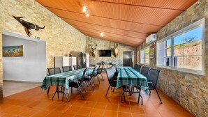 Un comedor con una mesa larga dispuesta para varias personas, paredes de piedra, techo de madera y vistas amplias a través de grandes ventanales.