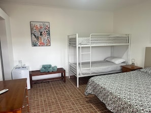Een slaapkamer met stapelbed, een bureau, een bankje en een aan de muur bevestigd schilderij.